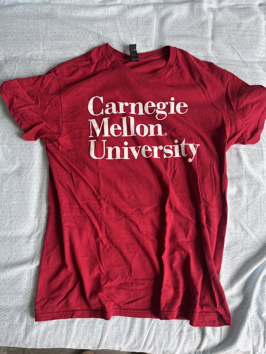 A red T-shirt laid flat on a bed, printed Carnegie Mellon University